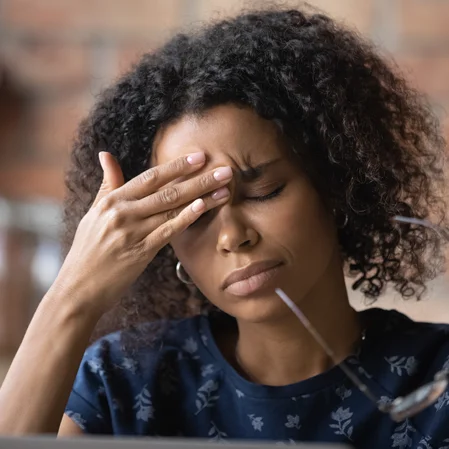 A woman taking off her glasses to rub her forehead, trying to alleviate a headache