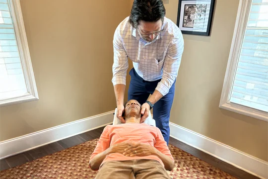 Dr. Thomas McKay Jr. performing a neck adjustment on a patient while the patient lays on an adjustment table